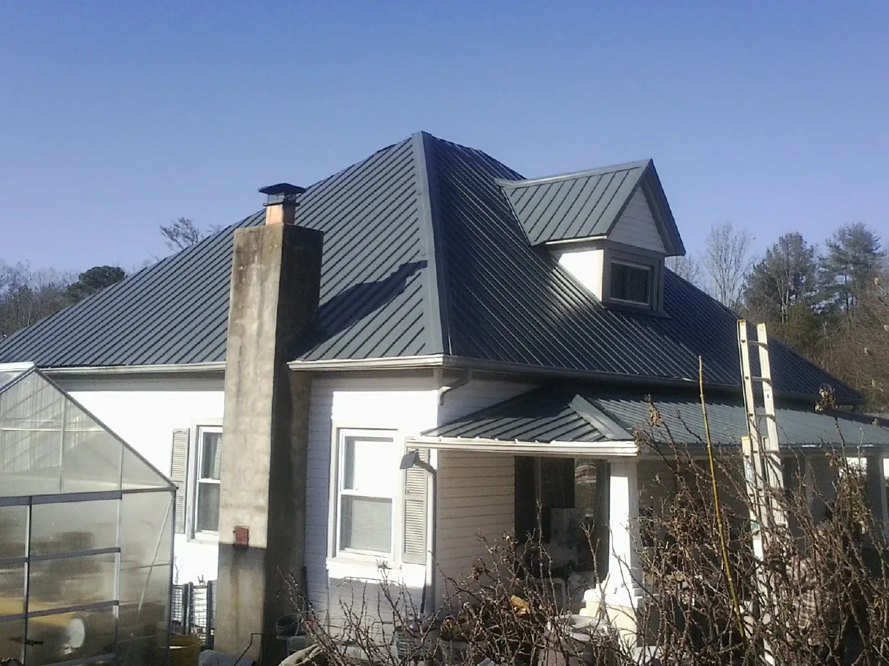 Dark blue standing seam metal roof on a white farmhouse with dormer — Slate & Tile Roof Repair by Roofing Brothers in Mount Arlington