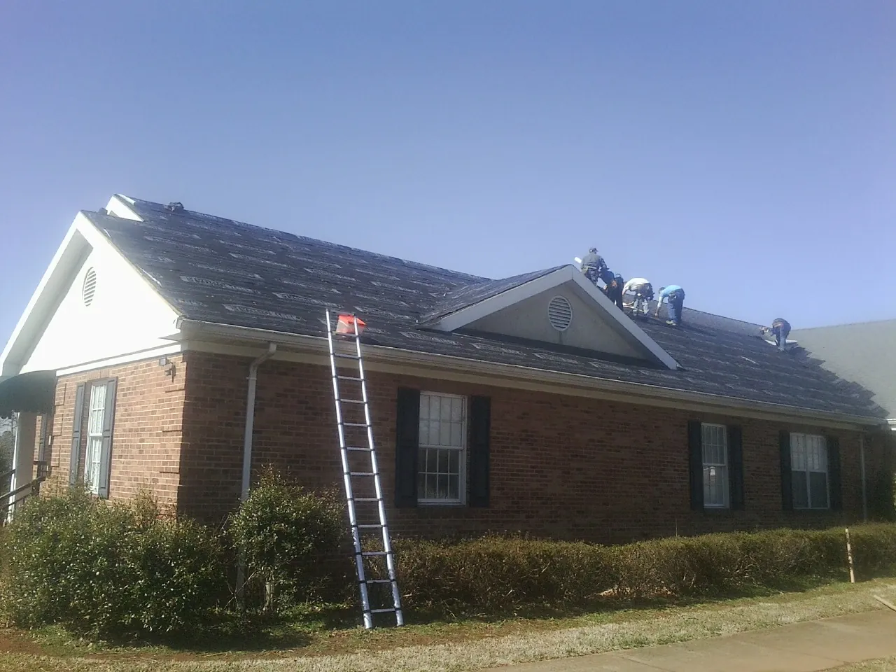 Crew tearing shingles off a brick ranch roof with a ladder set — Metal Roof Repair work by our crew in Mount Arlington