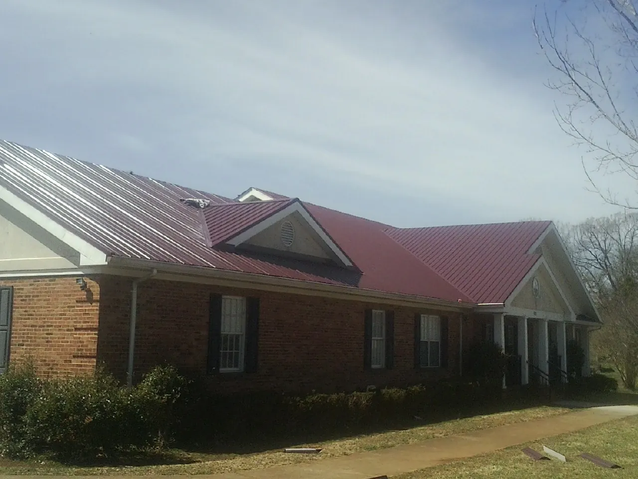 Red metal roof with gabled entries on a long brick building, from a Hail Damage Roof Repair job in Mount Arlington