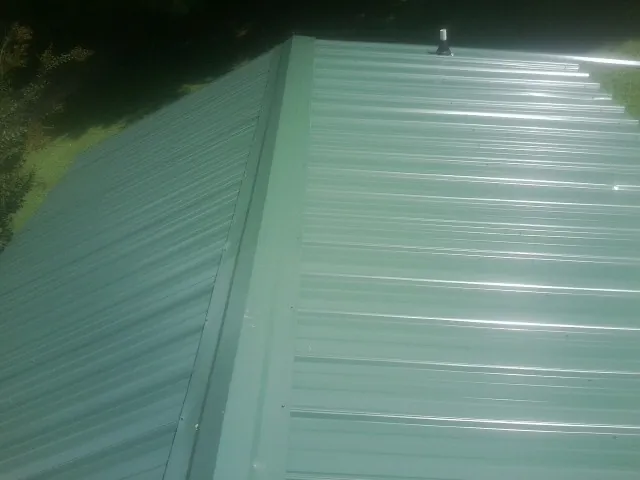 New green metal panels meeting at the ridge of a roof — Flat Roof Repair work by our crew in Mount Arlington