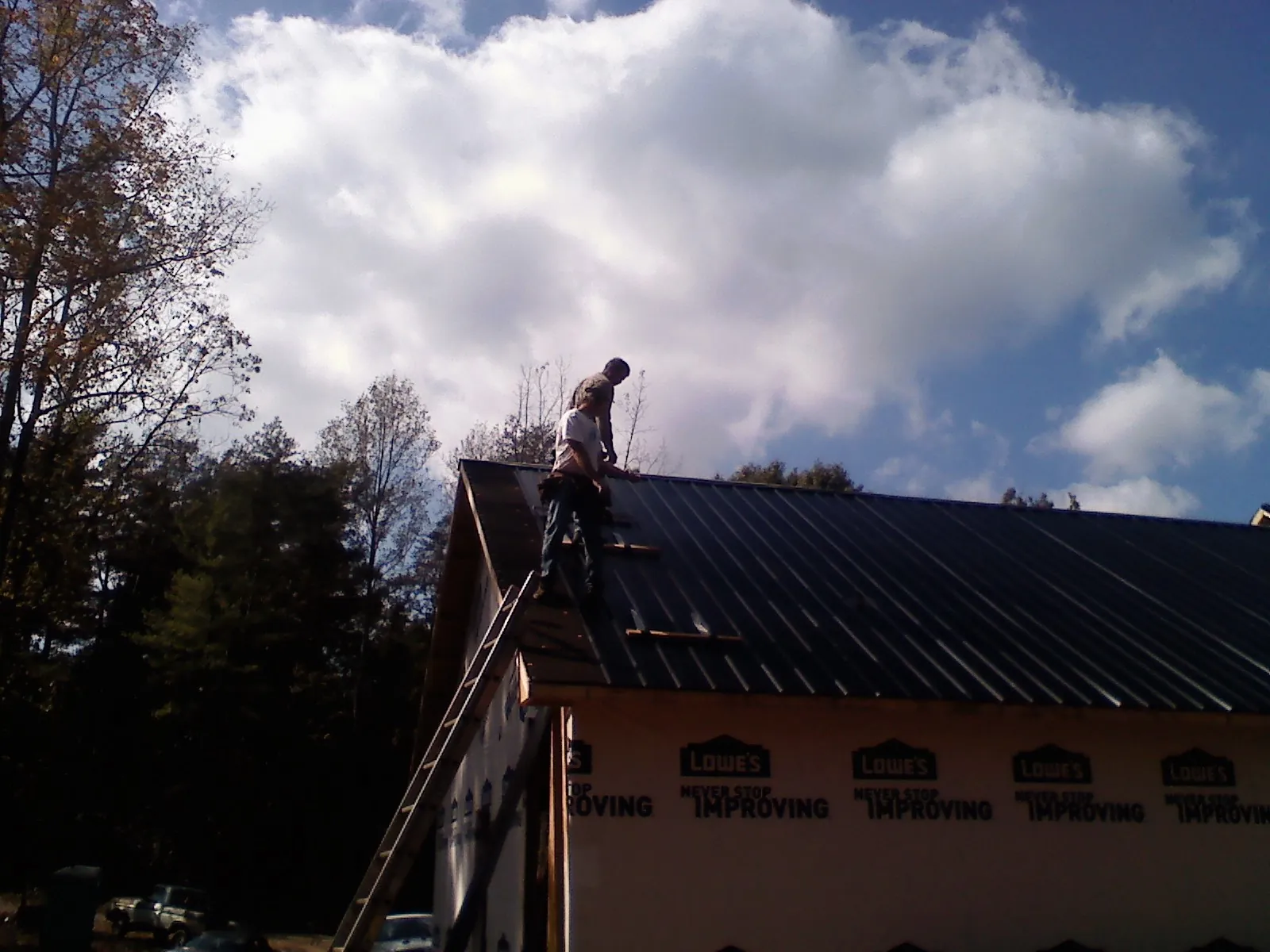 Roofer fastening dark metal panels high against a cloudy sky, from a Roof Inspection job in Mount Arlington
