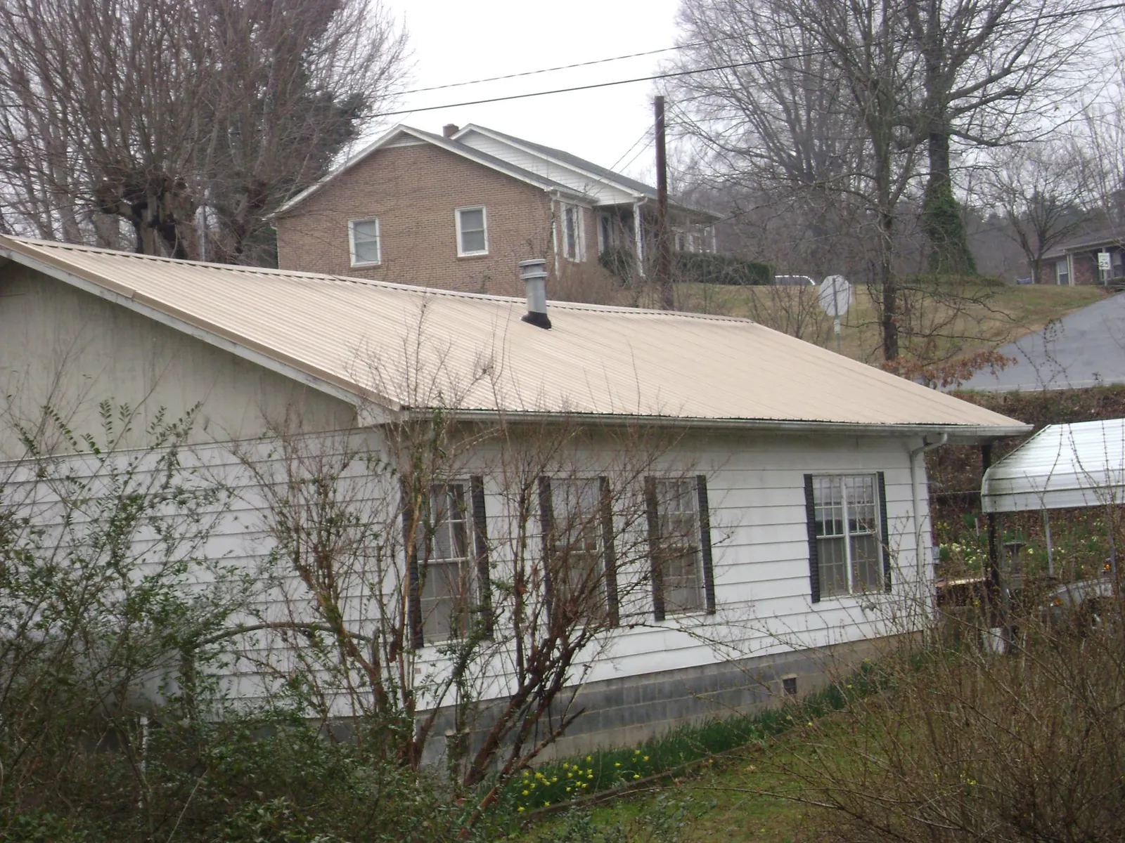 Tan metal roof on a white sided house set into a hillside — Commercial Roofing by Roofing Brothers in Mount Arlington